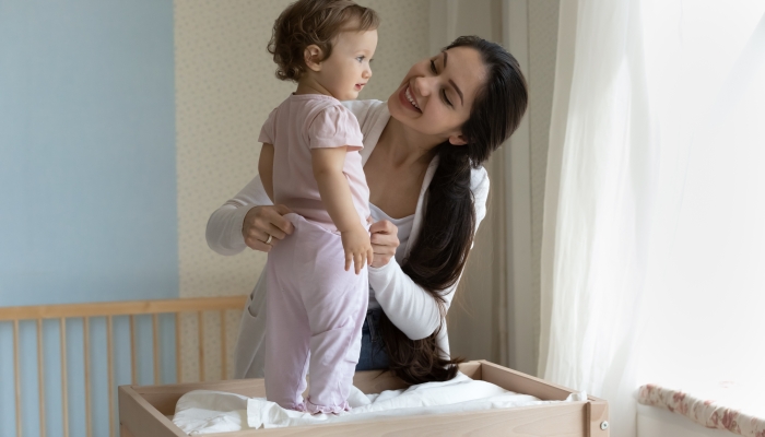 Happy young mom dressing cute toddler girl on baby changing table.