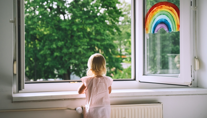 Little girl looks out open window at spring time.