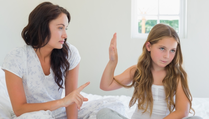 Little girl showing stop gesture to angry mother while sitting in bed at home.