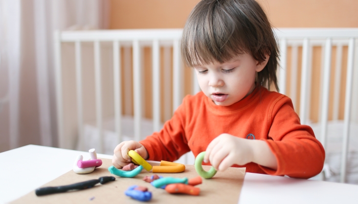 Lovely little boy playing with plasticine at home.