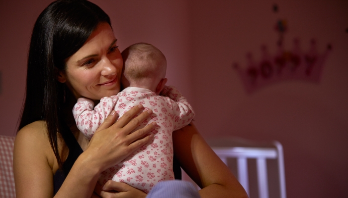 Mother At Home Cuddling Newborn Baby In Nursery.