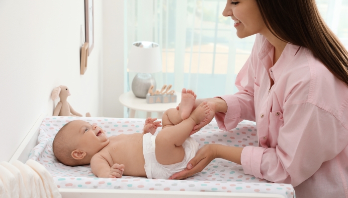 Mother changing her baby's diaper on table at home.