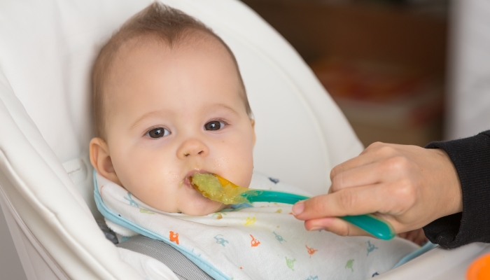 Mother feeding baby girl with mashed avocado.