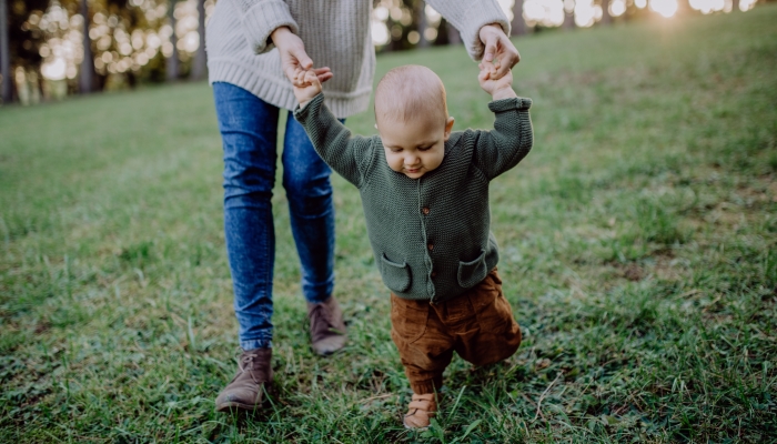 Mother holding hands of her baby son when walking in nature.