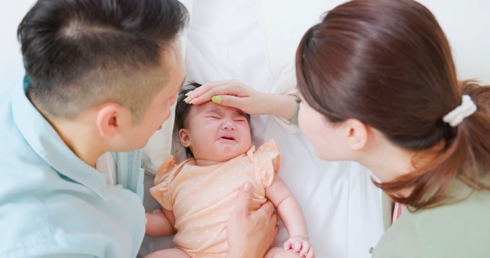 Parents lying on bed comforting crying baby.