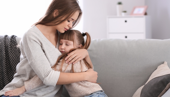 Sad woman hugging her little daughter while sitting on sofa.