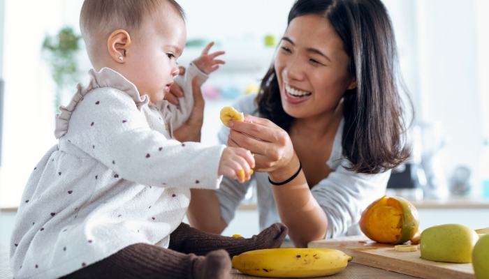 Shot of happy young mother feeding her cute baby girl with a banana in the kitchen at home.