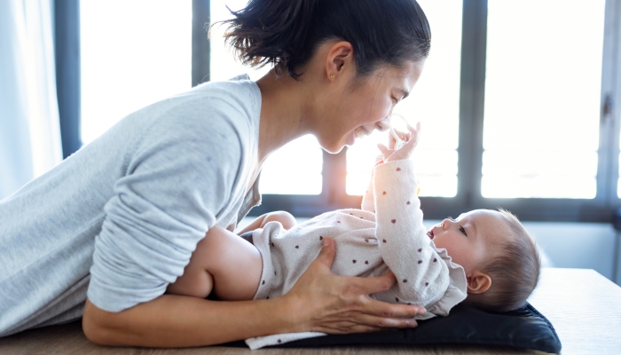 Shot of smiling young mother has fun with little baby while changing his nappy at home.