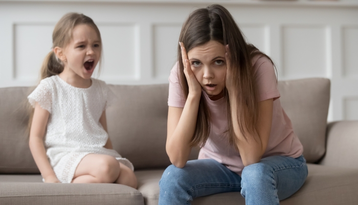 Stressed exhausted mother looking at camera feeling desperate about screaming stubborn kid.