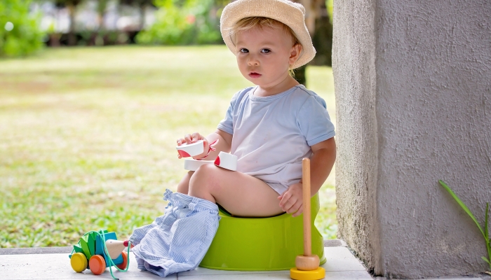 Sweet toddler boy, sitting on potty on a back porch in a holiday resort patio.