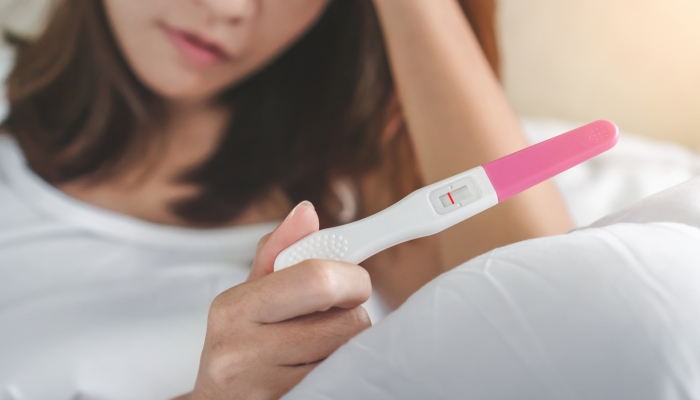 Unhappy young asian woman holding pregnancy test showing a negative result.