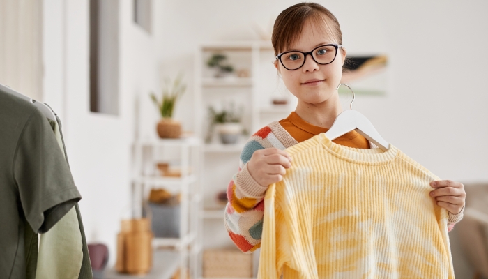 Waist up portrait of teenage girl with Down syndrome choosing clothes and looking at camera.