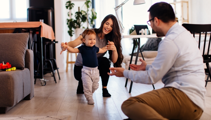 Young married couple teaching their son to learn the first baby steps in their home.