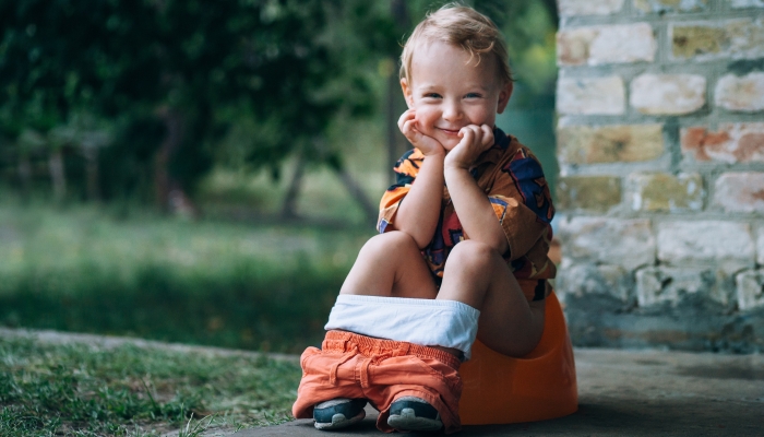 Little child sits on a pot in the garden.