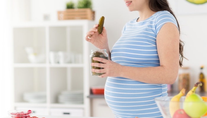 Pregnant woman eating pickled cucumber at home kitchen.