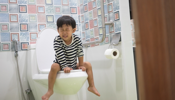 A boy is sitting on toilet.