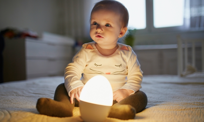 Adorable baby girl playing with bedside lamp in nursery.