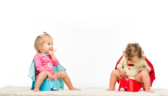 Adorable toddlers in superhero capes sitting on potties isolated on white.