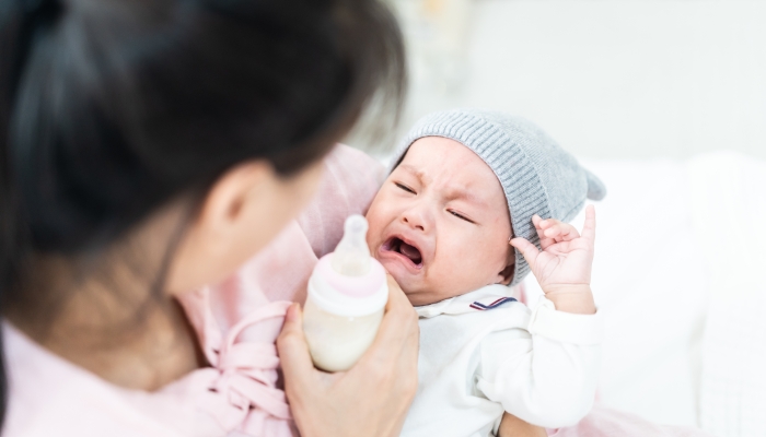 Asian mother holding and feeding crying baby from milk bottle.