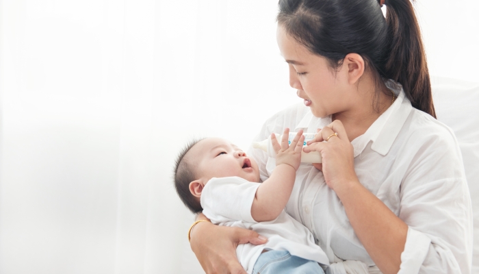 Baby is drinking milk from a bottle hold by the mother.