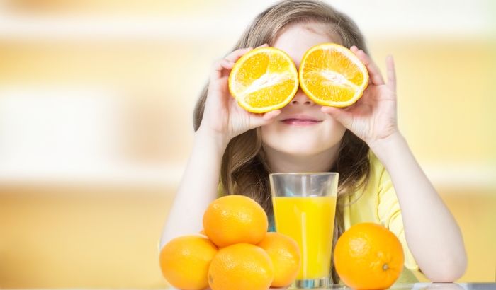 Child girl drinking glass of fresh orange juice indoors.
