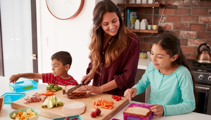 Children Helping Mother To Make School Lunches In Kitchen At Home.