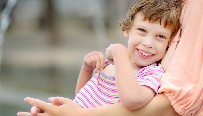 Close-up portrait of beautiful disabled girl in the arms of his mother having fun in fountain of public park at sunny summer day.