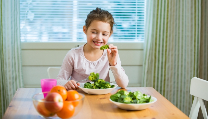 Cute girl eating spinach and broccoli at the table.