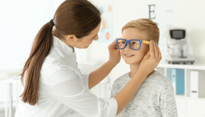 Cute little child trying on new glasses in ophthalmologist's office.