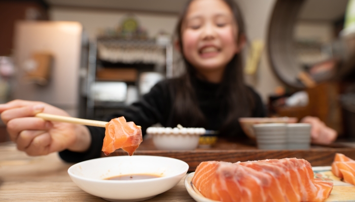 Girl eating sashimi with chopsticks.