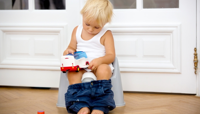 Infant child baby boy toddler sitting on potty, playing with toys in living room.