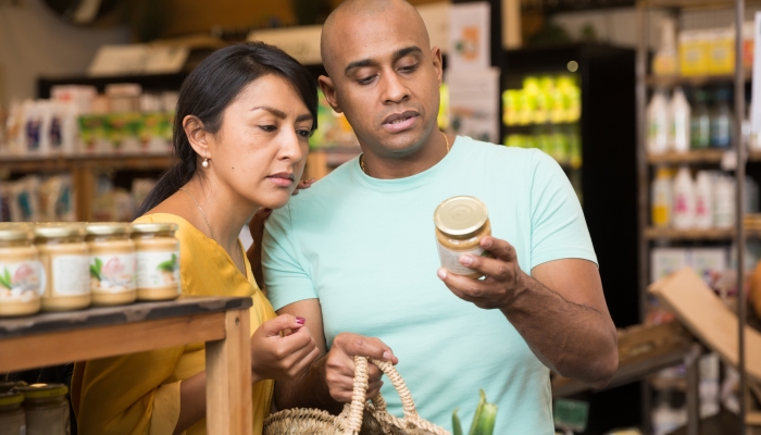 Interested Latin American couple reading product label on jar while choosing groceries in supermarket.