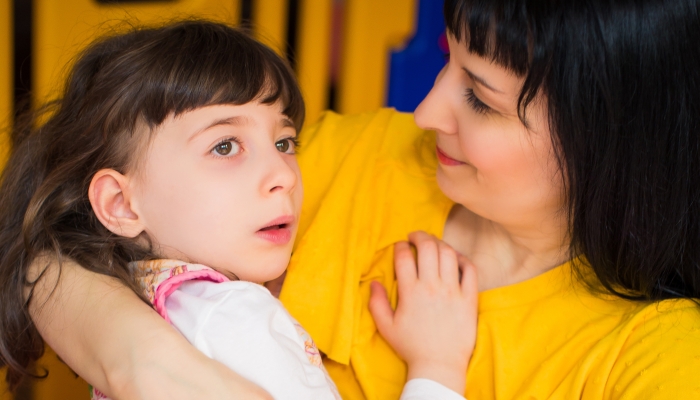 Portrait of little beautiful disabled girl who lying in her mother's arms in the room.