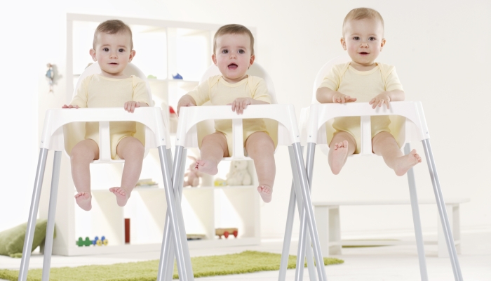 Triplet babies sitting in high chairs.