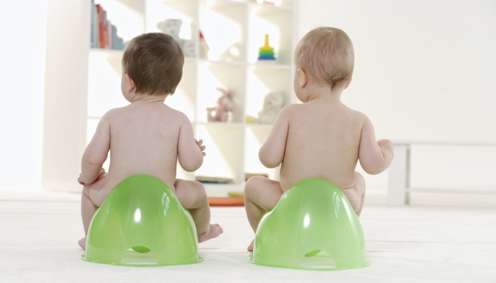 Two babies.sitting on potty chairs.