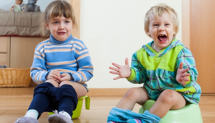 Two emotional siblings sitting on chamber pots in home interior.