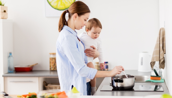 Happy mother and little baby girl cooking dinner together at home kitchen.
