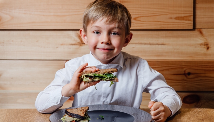 Little boy with vegetarian sandwich with whole grain bread, cucumber, egg whites, radishes and pea shoots on plate.