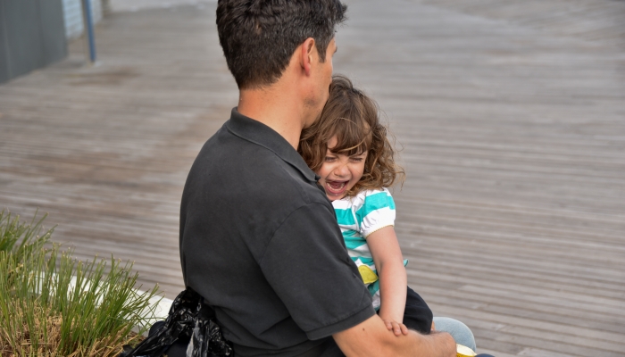 A distraught little girl cries on her father's lap.