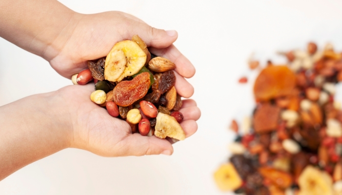 A little boy holds various dried fruits in his hands - bananas, apricots, raisins and also nuts, close up.