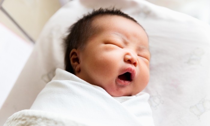 A portrait of sleepy cute newborn baby yawning 2 days after birth.