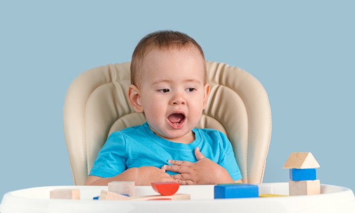 A surprised child with his mouth open looks at the wooden cube house.