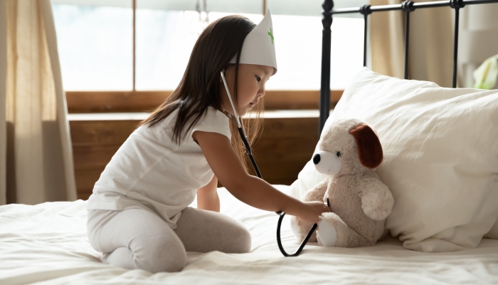 Adorable small vietnamese ethnicity child girl in nurse hat sitting on bed.