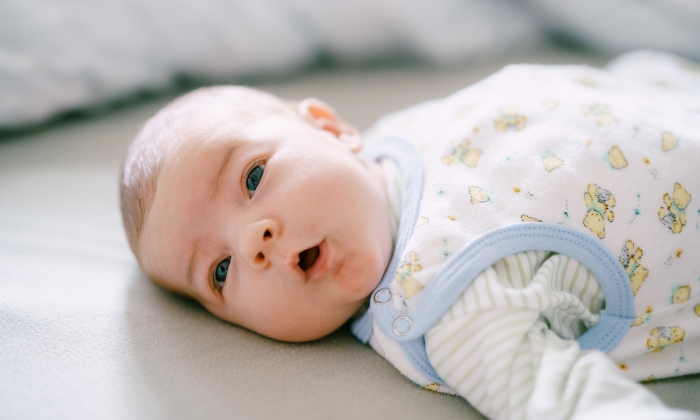 Baby lies on the bed with his head turned to the side and his mouth open.