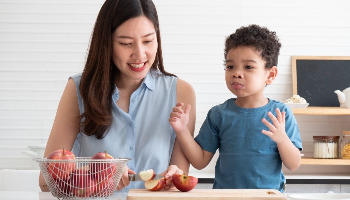 Beautiful Asian mom was slicing apples in the kitchen, with the mixed-race Asian-African boy on the side taking the sour apples to taste.