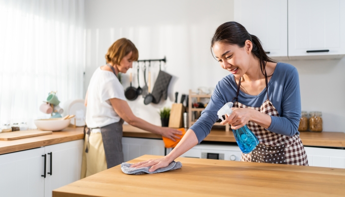 Caucasian senior elderly woman cleaning kitchen in house with daughter.