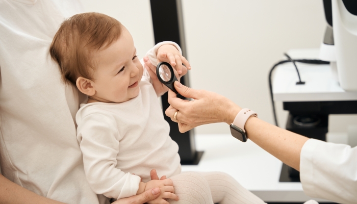 Experienced pediatric ophthalmologist examining baby eyes during consultation.