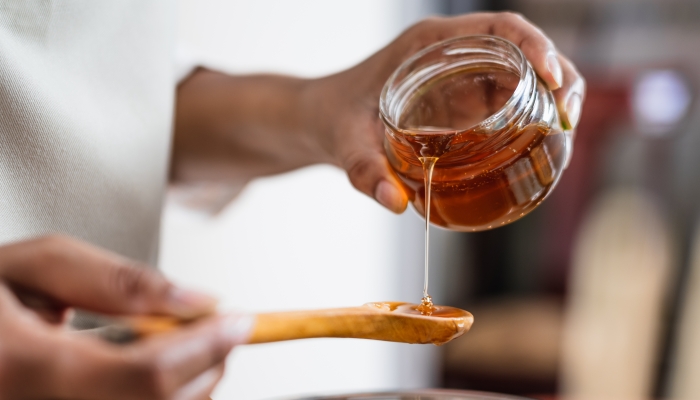 Female hands holding a bowl of bee honey and a wooden spoon.