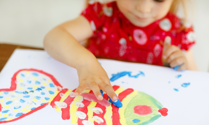 Little creative toddler girl painting with finger colors a fish.