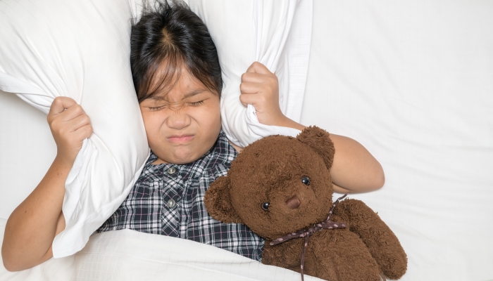 Little girl lying in bed covering head with pillow because too loud annoying noise.